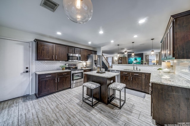 kitchen with appliances with stainless steel finishes, a sink, backsplash, a peninsula, and dark brown cabinetry