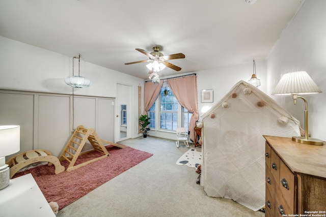 recreation room with carpet floors, ceiling fan, and a decorative wall