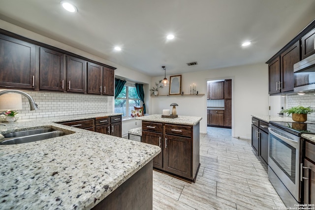 kitchen with appliances with stainless steel finishes, a sink, a kitchen island, dark brown cabinets, and recessed lighting