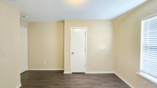 unfurnished room featuring dark wood-style flooring, baseboards, and a smoke detector