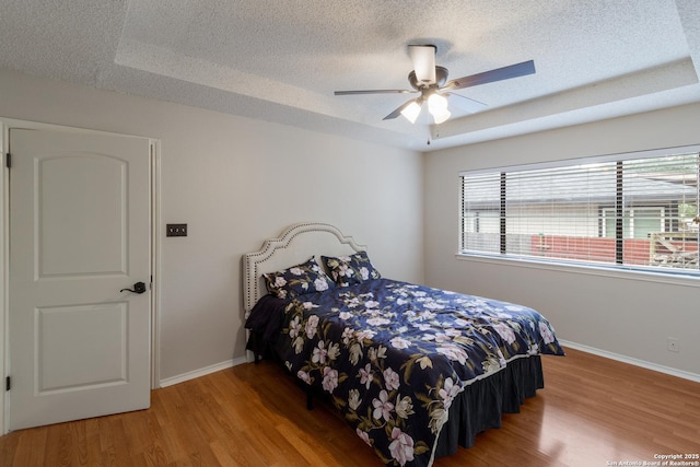 bedroom featuring wood finished floors, a textured ceiling, baseboards, a tray ceiling, and a ceiling fan