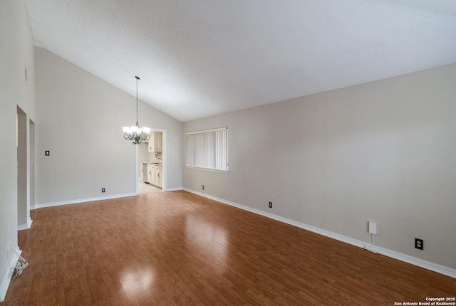 empty room featuring a chandelier, wood finished floors, baseboards, and high vaulted ceiling