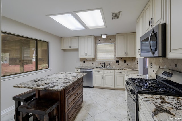kitchen with stainless steel appliances, a sink, backsplash, light stone counters, and light tile patterned flooring