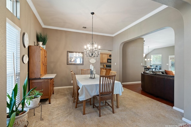 dining space featuring arched walkways, a chandelier, light colored carpet, and ornamental molding