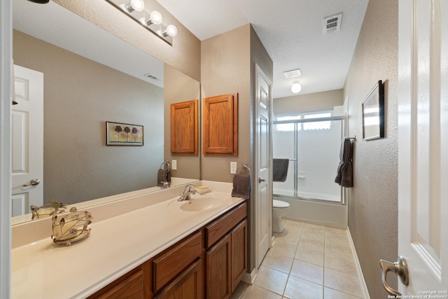full bathroom featuring a textured wall, tile patterned floors, vanity, combined bath / shower with glass door, and toilet
