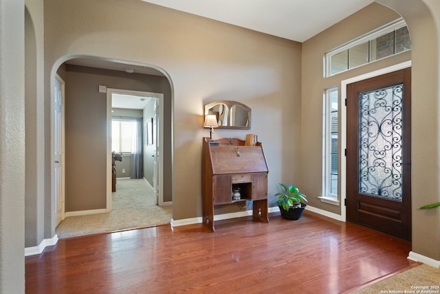entryway with arched walkways, wood finished floors, and baseboards