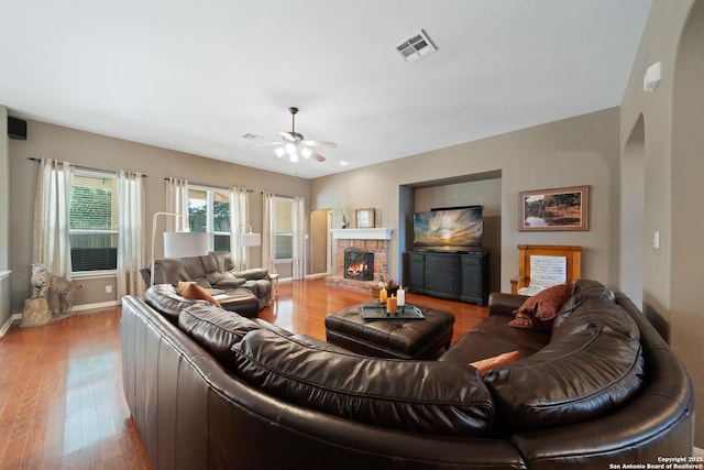 living area featuring light wood finished floors, a fireplace, a ceiling fan, and baseboards