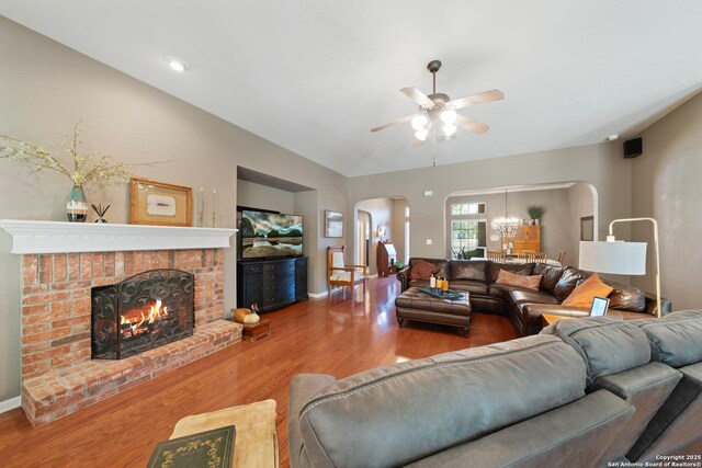 living room featuring arched walkways, ceiling fan, wood finished floors, a brick fireplace, and baseboards