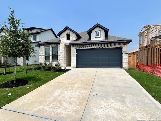 view of front of house with stone siding, a front yard, roof with shingles, a garage, and concrete driveway