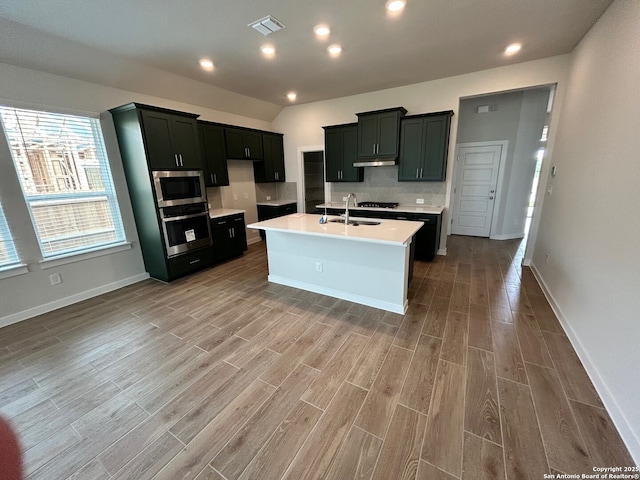 kitchen with appliances with stainless steel finishes, a sink, light wood finished floors, light countertops, and under cabinet range hood