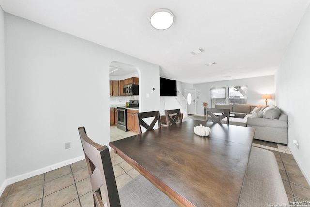 dining area featuring arched walkways, baseboards, and light tile patterned floors