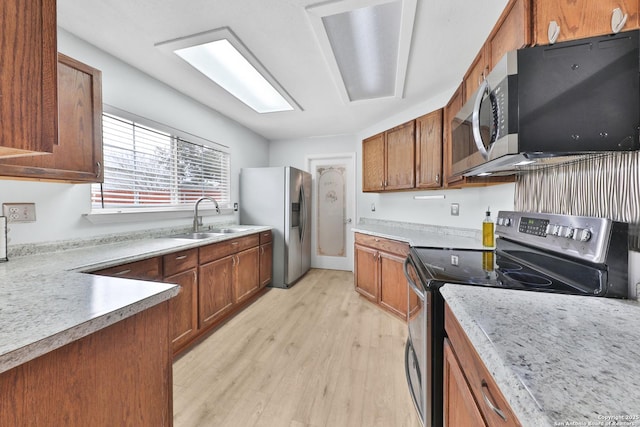 kitchen with stainless steel appliances, a sink, light wood-style floors, brown cabinets, and light countertops