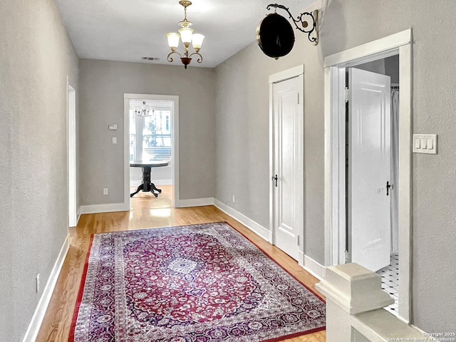 foyer entrance featuring light wood-type flooring, a chandelier, baseboards, and a textured wall