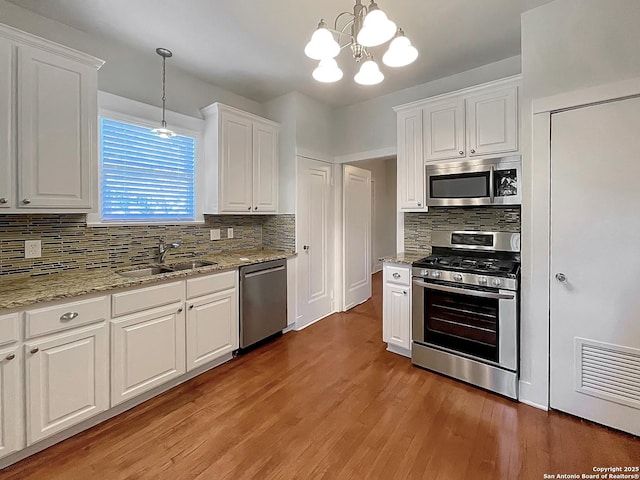 kitchen with stainless steel appliances, a sink, tasteful backsplash, white cabinetry, and a chandelier