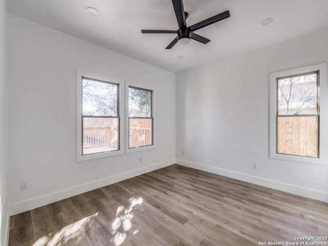 empty room featuring plenty of natural light, a ceiling fan, wood finished floors, and baseboards