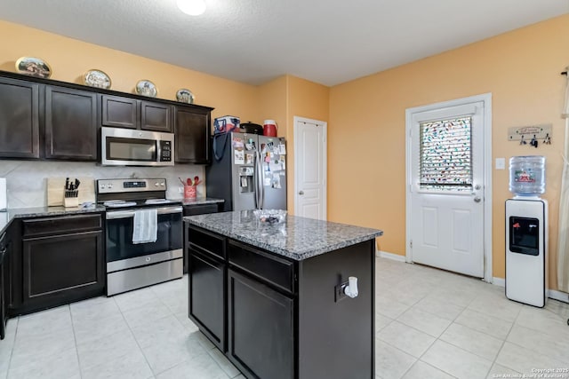 kitchen featuring appliances with stainless steel finishes, a center island, dark stone countertops, light tile patterned floors, and baseboards