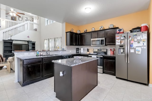kitchen featuring appliances with stainless steel finishes, a center island, light stone countertops, open floor plan, and a peninsula