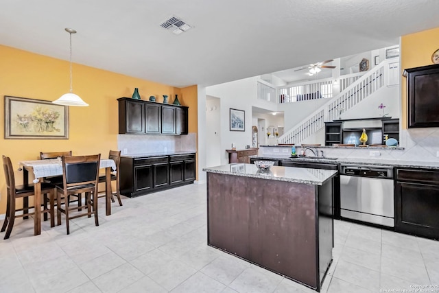 kitchen featuring stainless steel dishwasher, a center island, backsplash, a ceiling fan, and light stone countertops