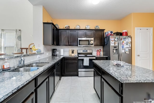 kitchen with stainless steel appliances, a sink, light stone counters, a kitchen island, and light tile patterned floors