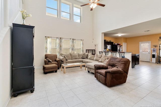 living room featuring a towering ceiling, light tile patterned flooring, ceiling fan, and baseboards