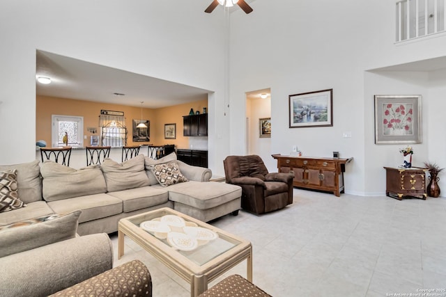 living area featuring ceiling fan, a towering ceiling, light tile patterned floors, and baseboards