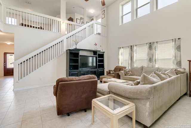 living room with a towering ceiling, stairs, ceiling fan, tile patterned floors, and baseboards