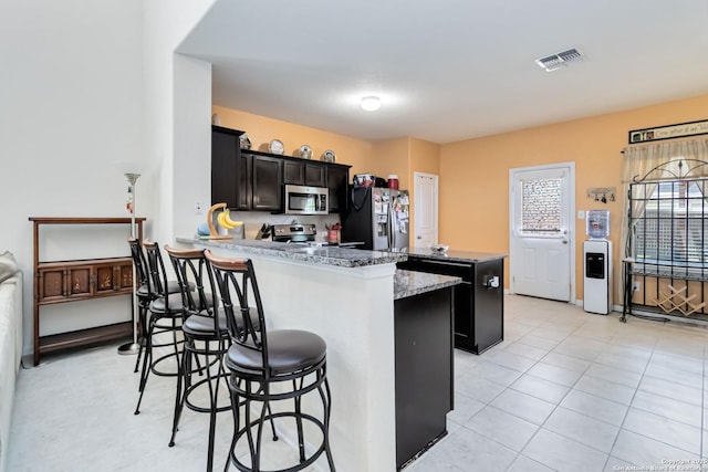 kitchen with appliances with stainless steel finishes, a breakfast bar, a peninsula, dark cabinets, and a kitchen island