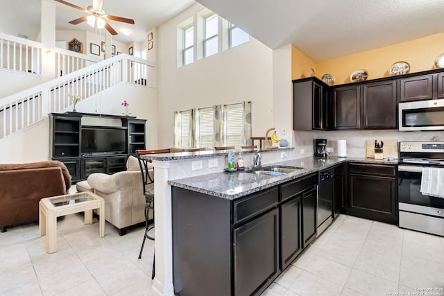 kitchen featuring appliances with stainless steel finishes, a sink, light tile patterned floors, dark stone counters, and a high ceiling