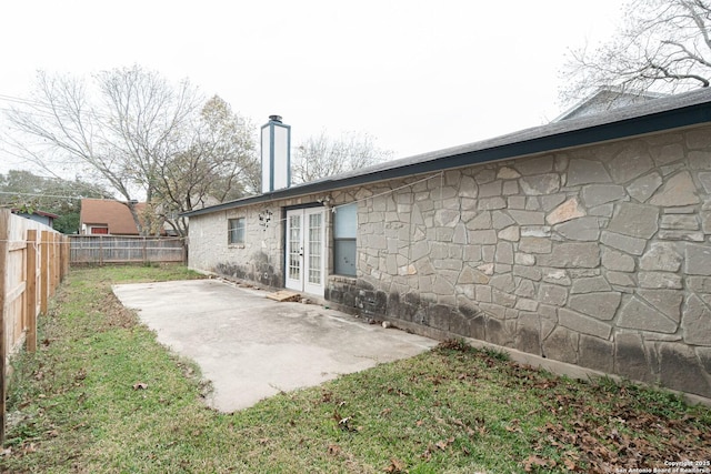 rear view of house with french doors, fence, a patio, a chimney, and stone siding