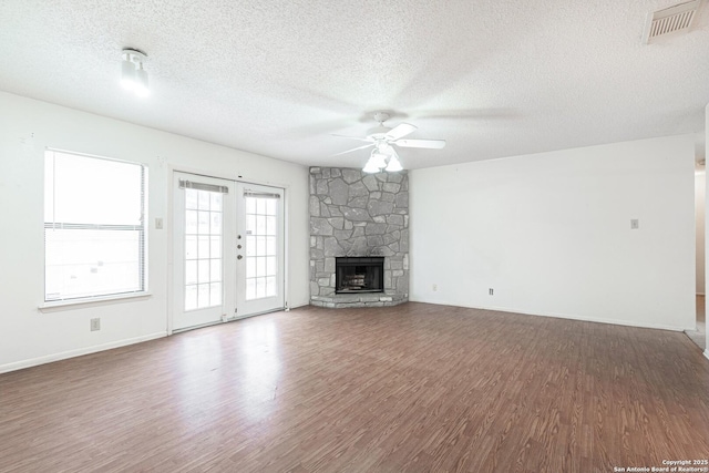 unfurnished living room with ceiling fan, a textured ceiling, wood finished floors, baseboards, and a fireplace