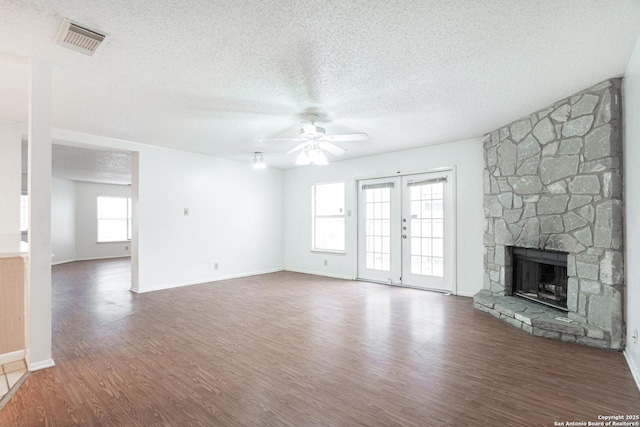 unfurnished living room featuring a ceiling fan, wood finished floors, a textured ceiling, a stone fireplace, and baseboards