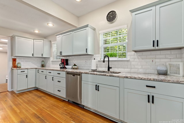 kitchen featuring dishwasher, a sink, backsplash, light wood finished floors, and light stone countertops