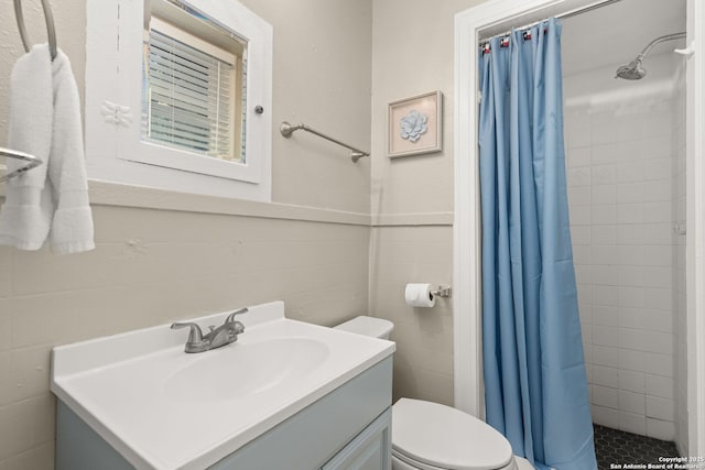 bathroom featuring toilet, a stall shower, vanity, tile walls, and wainscoting