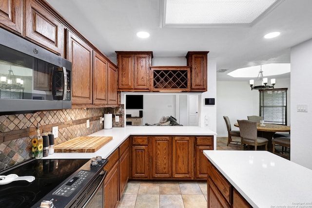kitchen featuring stainless steel microwave, range with electric stovetop, decorative backsplash, light countertops, and a chandelier