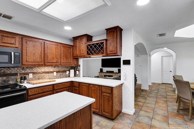 kitchen with stainless steel microwave, black / electric stove, light countertops, arched walkways, and backsplash