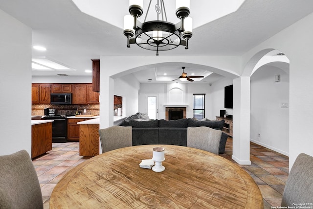 dining room featuring a ceiling fan, a tray ceiling, a chandelier, baseboards, and a fireplace