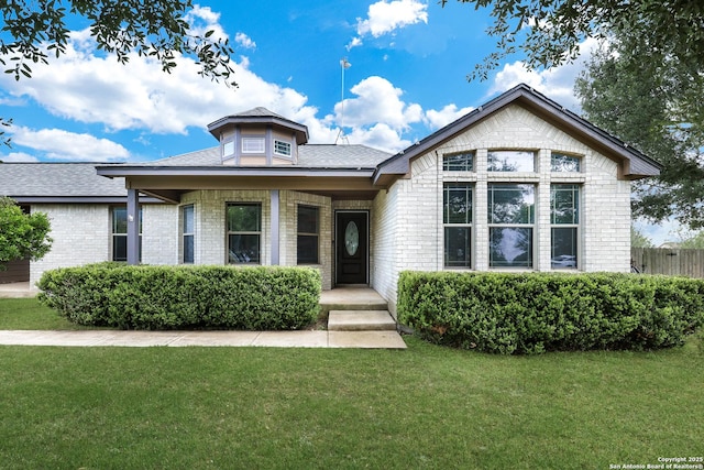 view of front of house with a front lawn, brick siding, and roof with shingles