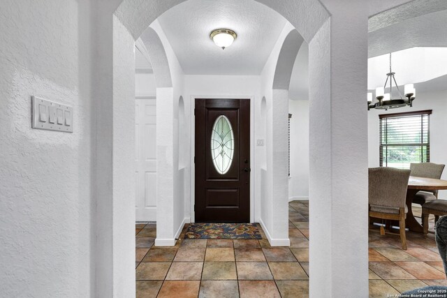 entrance foyer featuring a textured wall, a chandelier, baseboards, and arched walkways