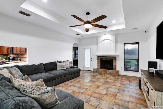 living room featuring a raised ceiling, a ceiling fan, a tile fireplace, arched walkways, and recessed lighting