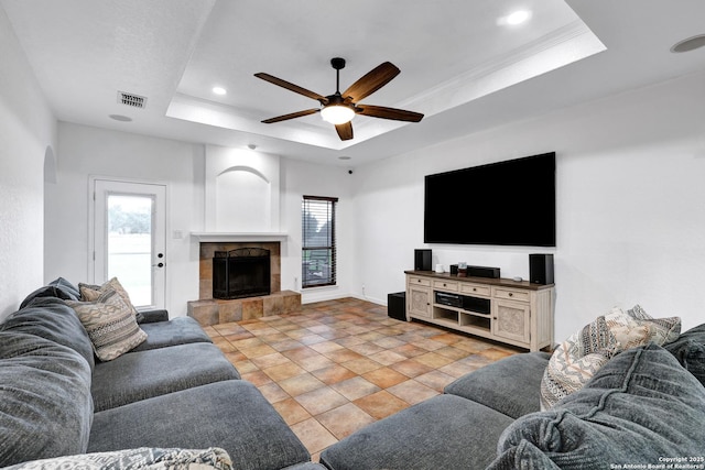 living area featuring a raised ceiling, ceiling fan, a tiled fireplace, arched walkways, and recessed lighting