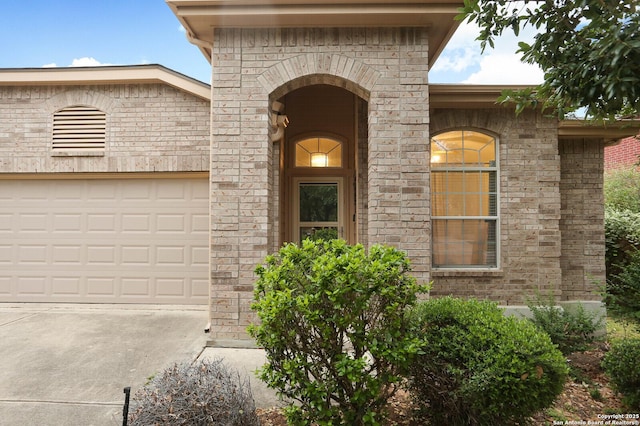 entrance to property with driveway, stone siding, and an attached garage