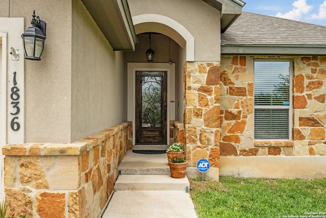 doorway to property with stone siding, a shingled roof, and stucco siding