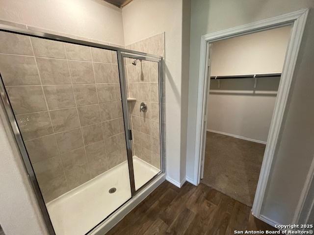 bathroom featuring a shower stall, wood finished floors, a spacious closet, and baseboards