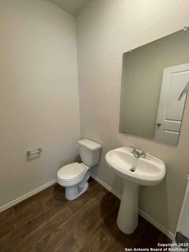half bathroom featuring wood finished floors, toilet, and baseboards