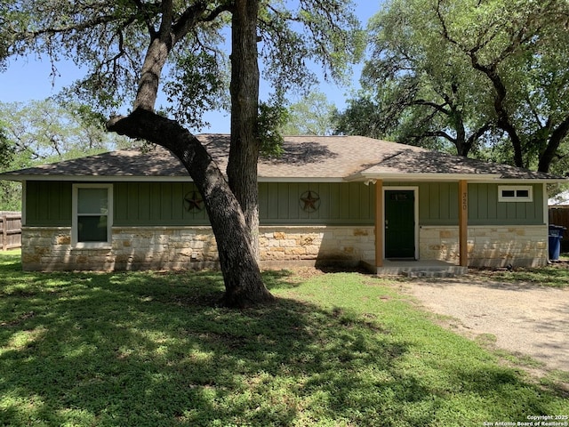 view of front of home with stone siding, a shingled roof, a front yard, and board and batten siding