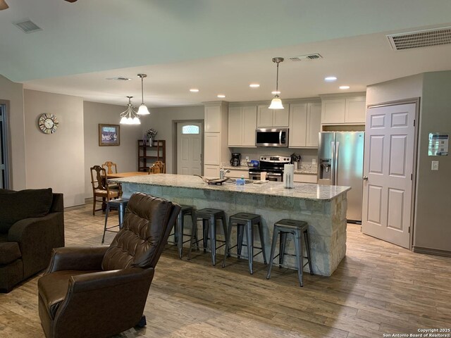 kitchen with stainless steel appliances, a kitchen bar, light wood-type flooring, open floor plan, and an island with sink