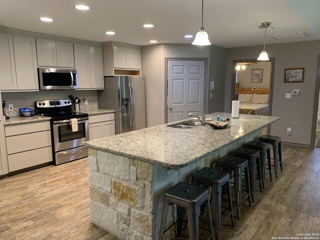 kitchen featuring appliances with stainless steel finishes, a sink, light wood-type flooring, a breakfast bar, and a center island with sink