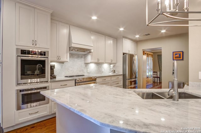 kitchen with appliances with stainless steel finishes, custom range hood, a sink, recessed lighting, and tasteful backsplash