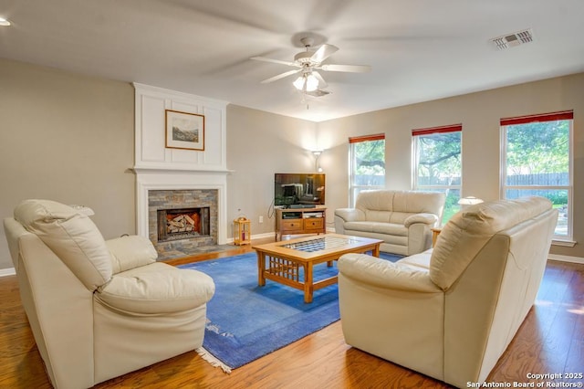 living room with ceiling fan, wood finished floors, a stone fireplace, and baseboards