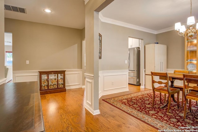 dining space with light wood-style flooring, a chandelier, a wainscoted wall, ornamental molding, and recessed lighting